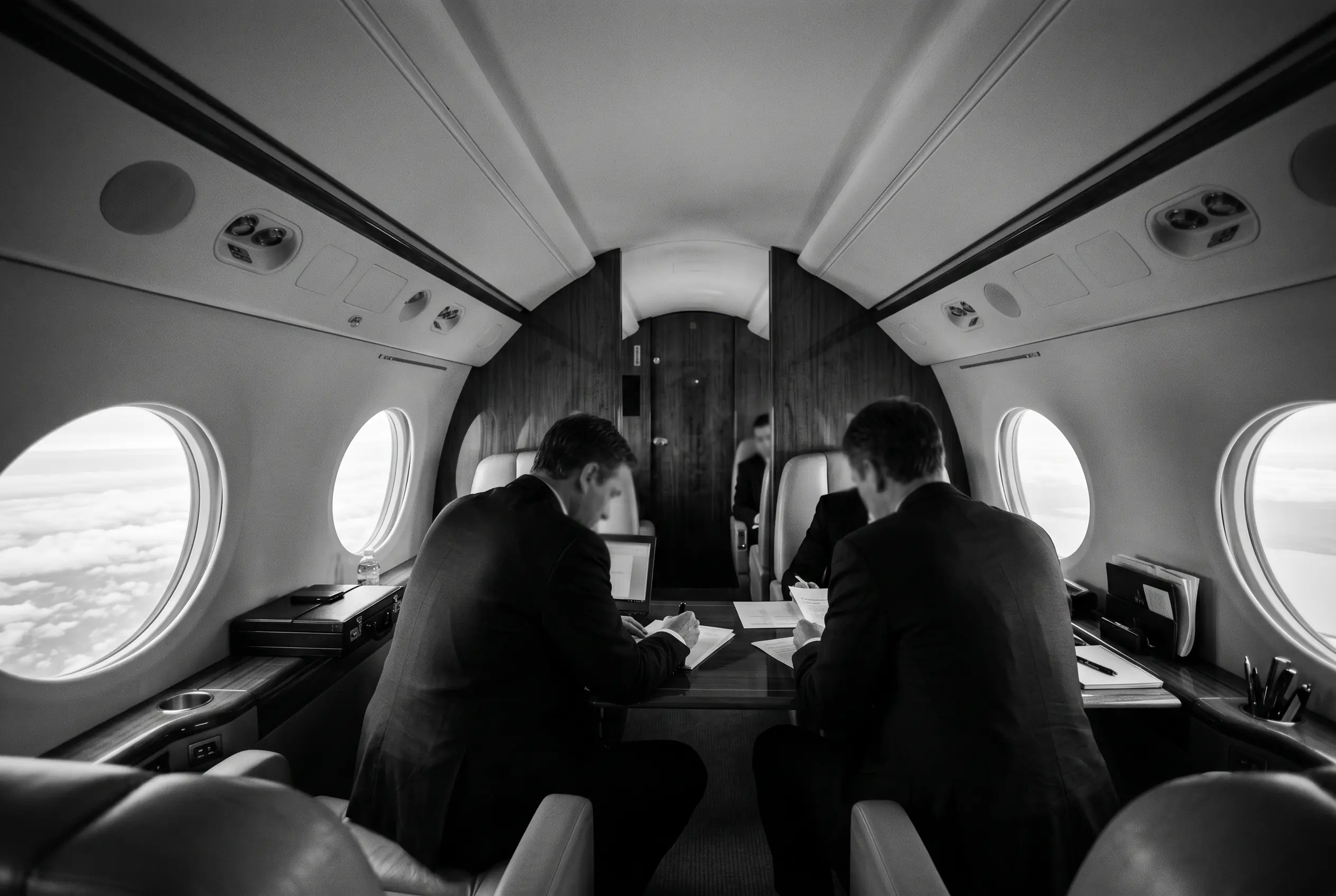Executives working at a worktable in a business jet cabin from New York to Miami, in monochrome