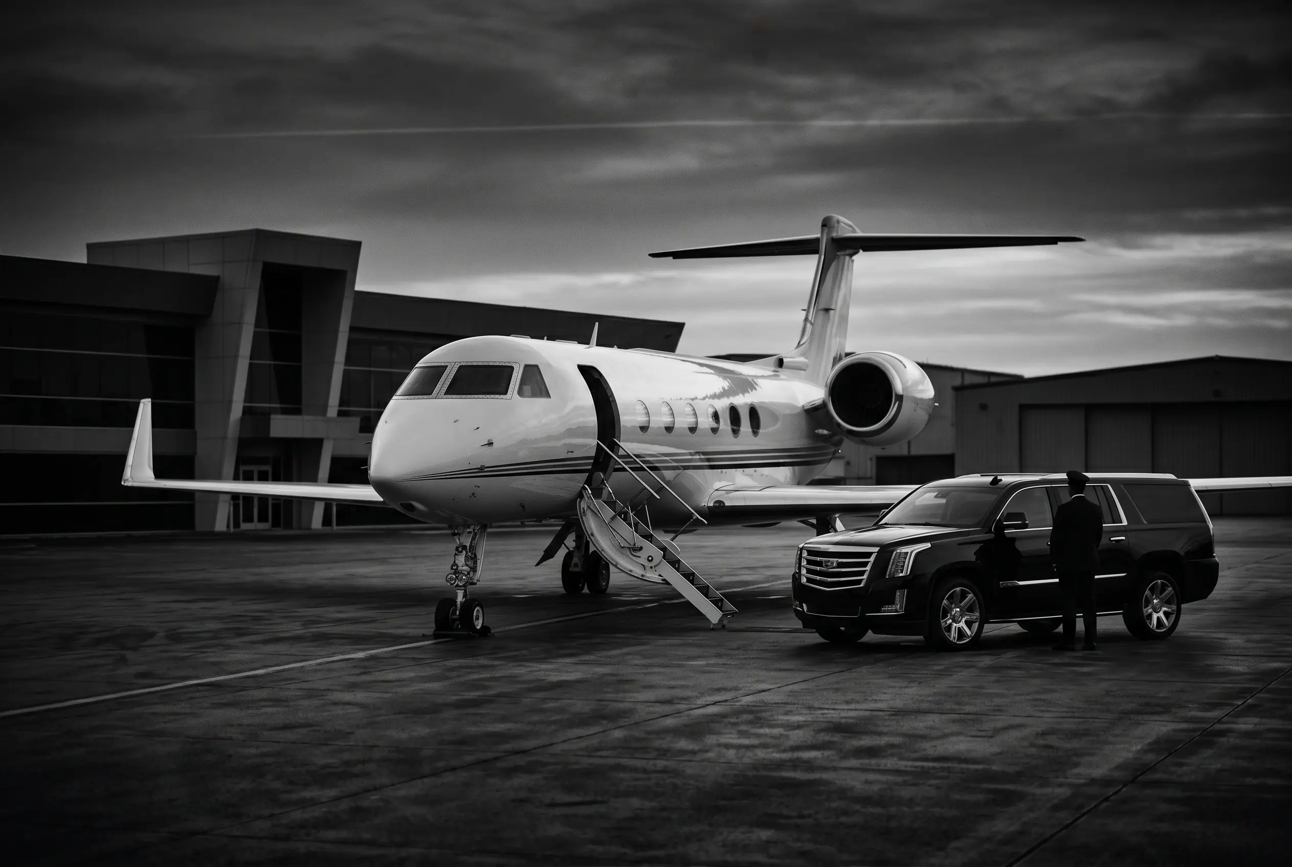 A chauffeured SUV waiting beside a private jet at a Miami FBO, in monochrome