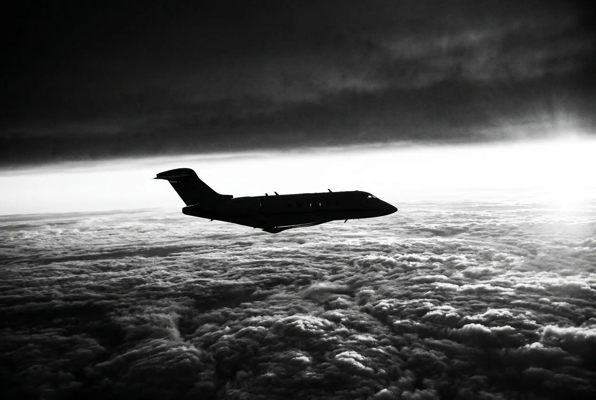 Private jet silhouetted in flight above a dramatic cloud layer